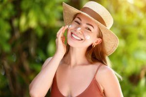Smiling woman with straw hat applying sunscreen to her face