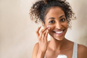 young black woman applying face cream on beige background